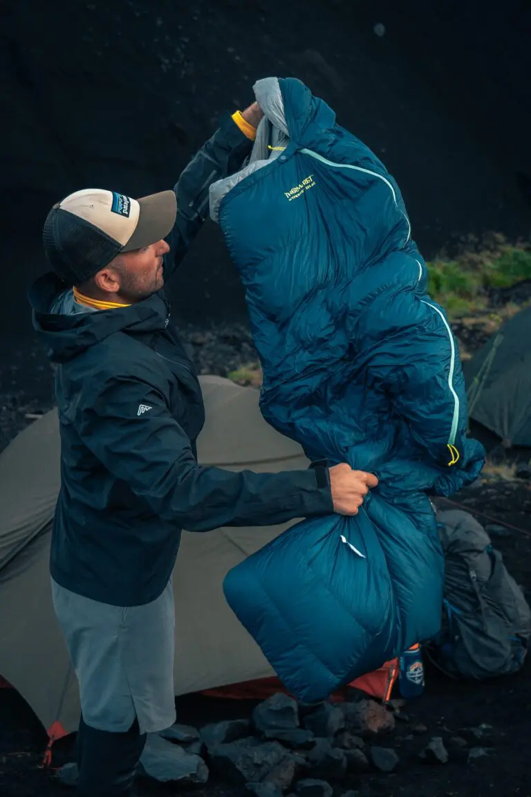 man packing a blue sleeping bag outside a tent